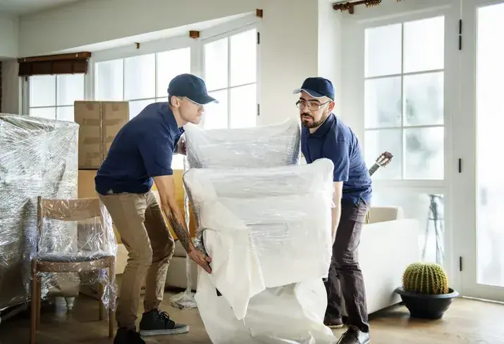 Two technicians wrapping pieces of furniture in stretch film before the move