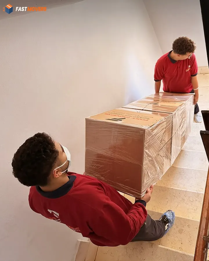 Two workers carrying a wrapped piece of furniture down the stairs