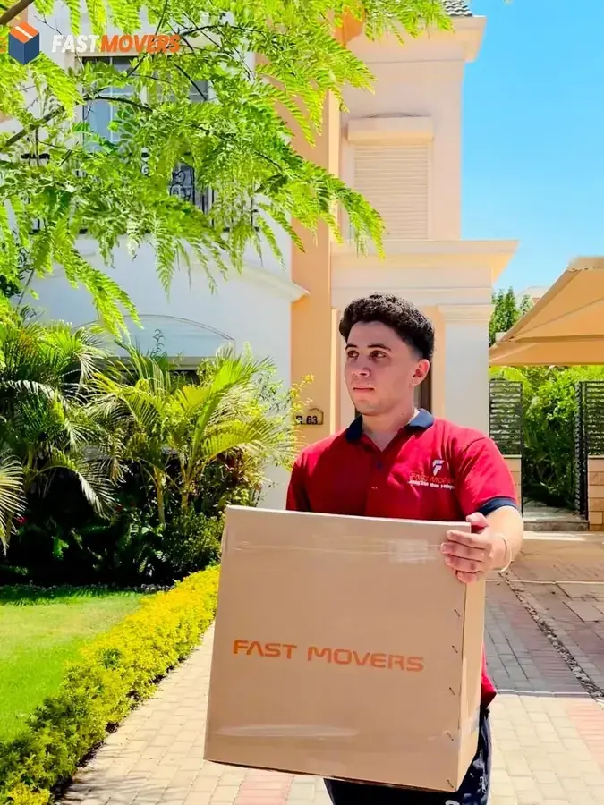 عامل يحمل كرتونة عليها شعار Fast Movers أمام فيلا