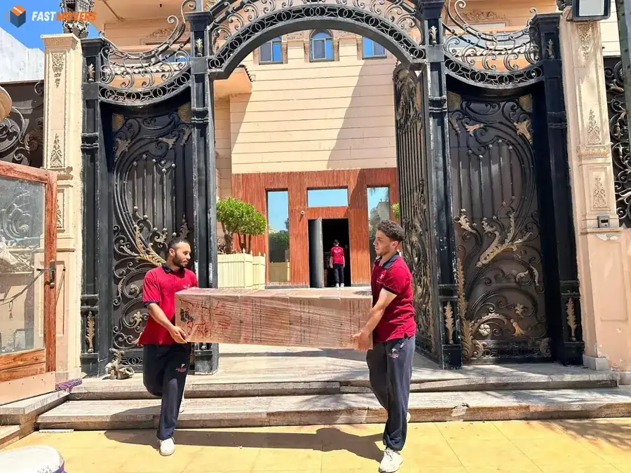 Two Fast Movers workers carrying a wrapped piece of furniture in front of a villa gate